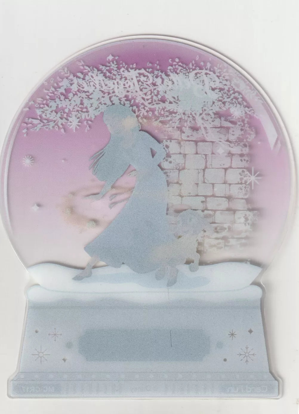 A translucent die-cut snow globe card back showing Asha and Valentino in a snowy scene, with soft purples and whites in the background.