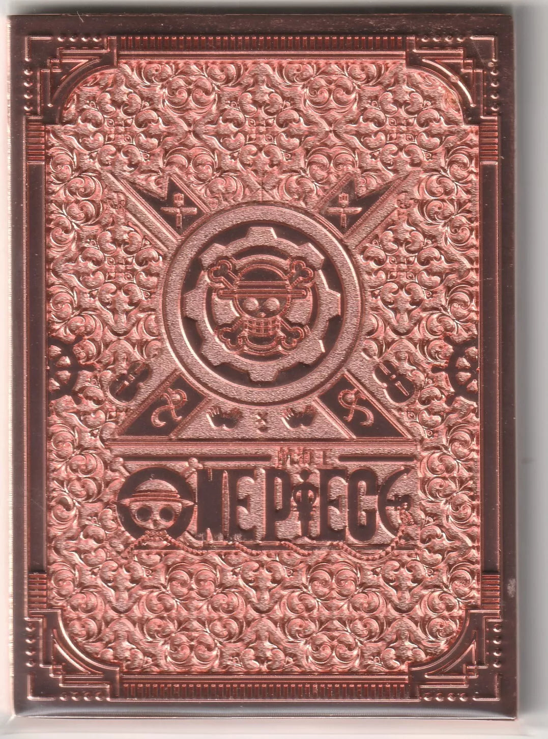 The back of an anime card with ornate, swirling rose-gold engravings and a central One Piece emblem in a metallic finish.