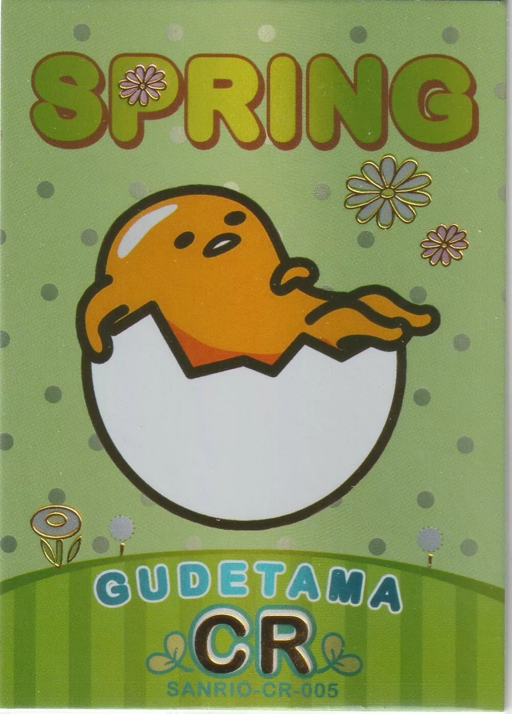 Gudetama lounging in an eggshell with "SPRING" in large letters, surrounded by flowers, on a green background with foil accents.