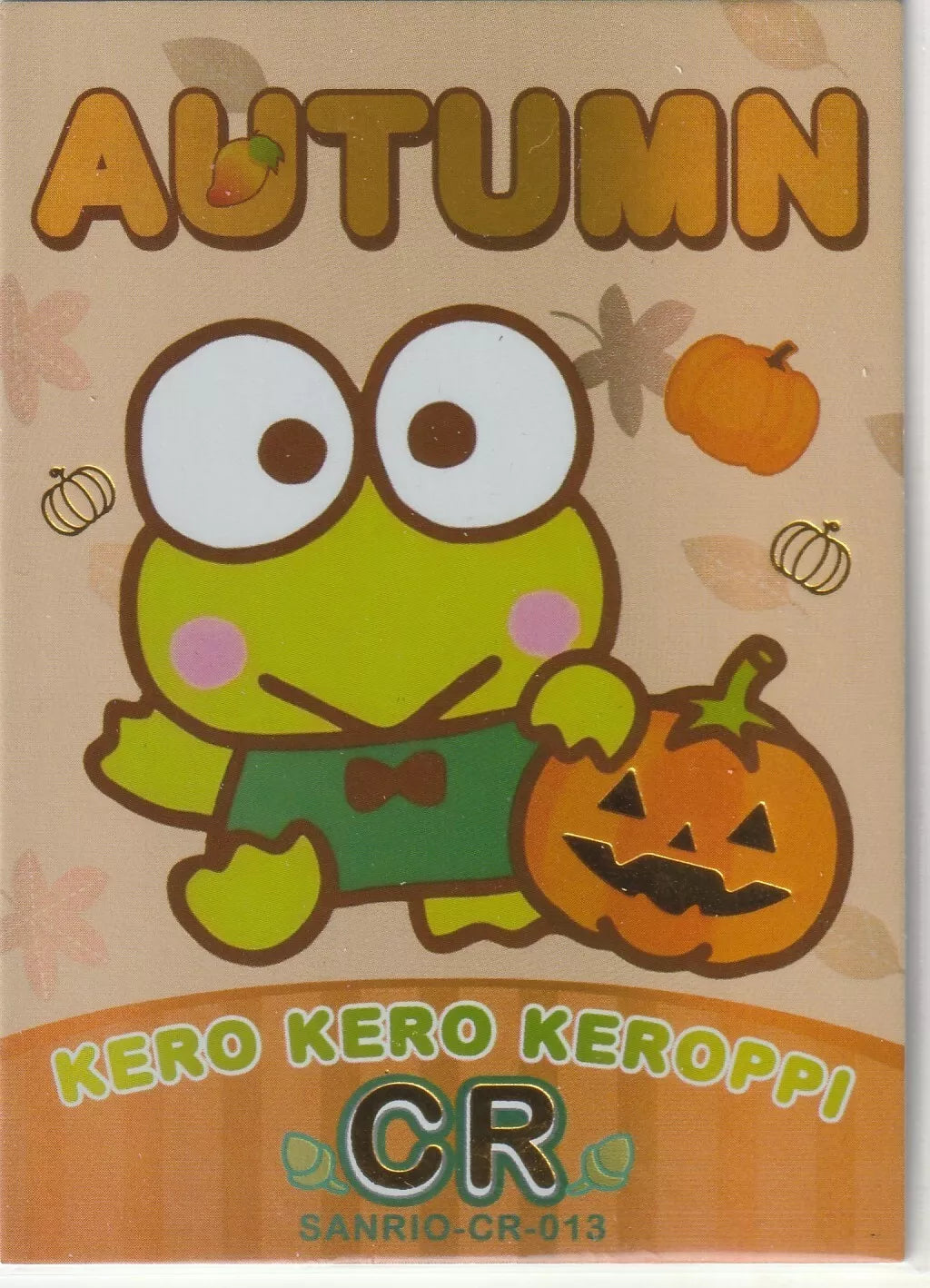 Kero Kero Keroppi from Sanrio with a jack-o'-lantern, dressed in a green bowtie, surrounded by fall leaves and pumpkins with foil accents.