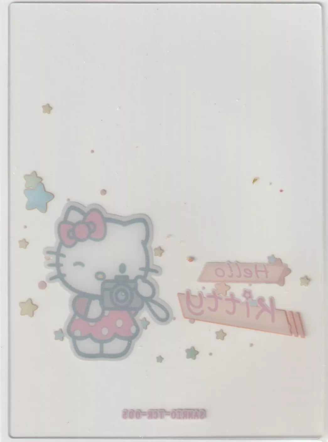 Hello Kitty collectible card back with a reversed image of Hello Kitty holding a camera, pastel stars, and mirrored text, all slightly faded due to the card's transparency.