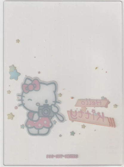 Hello Kitty collectible card back with a reversed image of Hello Kitty holding a camera, pastel stars, and mirrored text, all slightly faded due to the card's transparency.